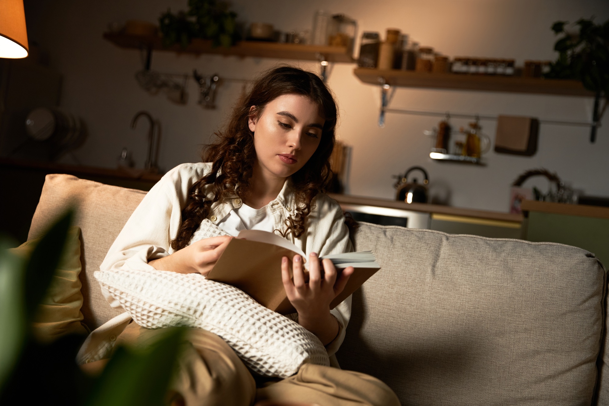 Cozy moments of a beautiful young woman enjoying a book at home in the evening light